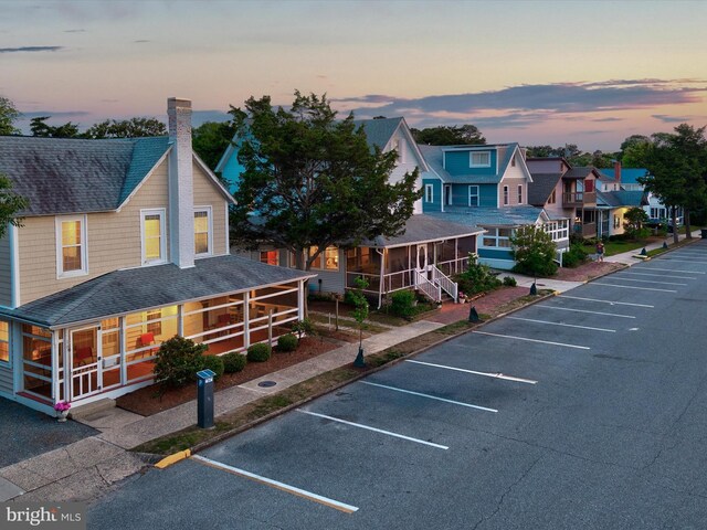 16 Delaware Ave, Rehoboth Beach, DE 19971 - back of house at dusk with uncovered parking, a chimney, roof with shingles, a sunroom, and a residential view