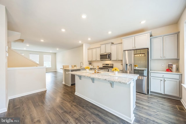 402 Monte Farm Rd, Mount Laurel, NJ 08054 - kitchen with stainless steel appliances, a kitchen island with sink, a breakfast bar area, dark wood-type flooring, and light stone counters