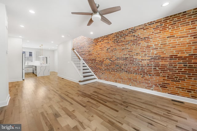 267 S Ellwood Ave, Baltimore, MD 21224 - unfurnished living room featuring baseboards, light wood-style flooring, a ceiling fan, brick wall, and stairs