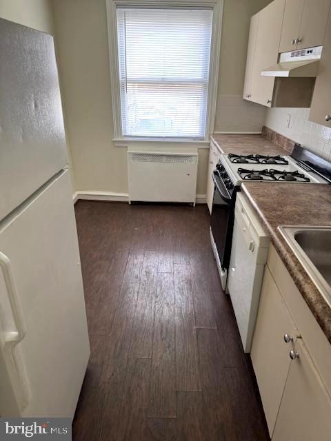 7113 Castor Ave, Philadelphia, PA 19149 - kitchen featuring white appliances, under cabinet range hood, radiator heating unit, dark wood finished floors, and white cabinets