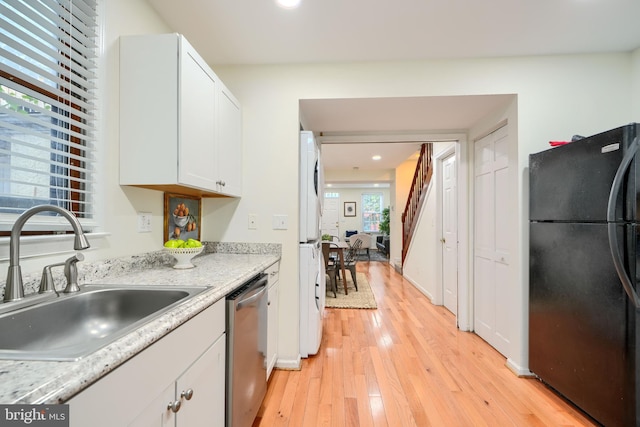 106 W Montgomery St, Baltimore, MD 21230 - kitchen featuring freestanding refrigerator, stainless steel dishwasher, stacked washing machine and dryer, light wood finished floors, and white cabinets