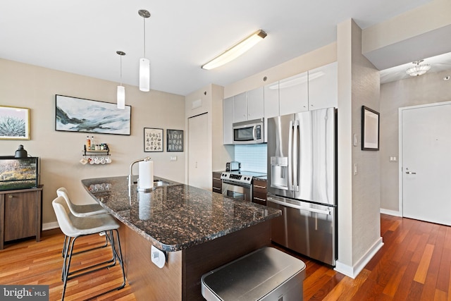 2101 Market St Unit 1104, Philadelphia, PA 19103 - kitchen featuring appliances with stainless steel finishes, white cabinets, wood finished floors, a kitchen bar, and hanging light fixtures