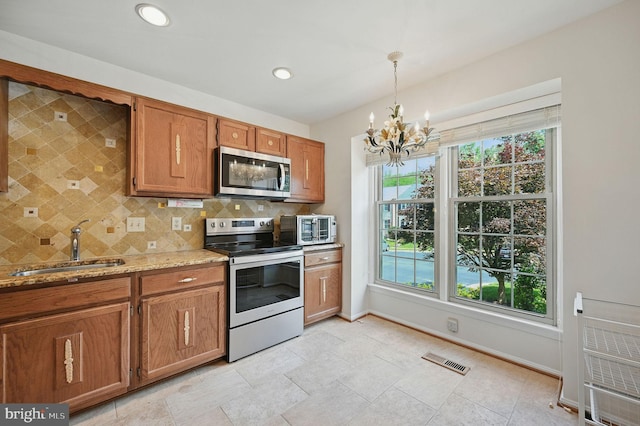 11707 Critton Cir, Woodbridge, VA 22192 - kitchen with stainless steel appliances, brown cabinets, a chandelier, backsplash, and light stone counters