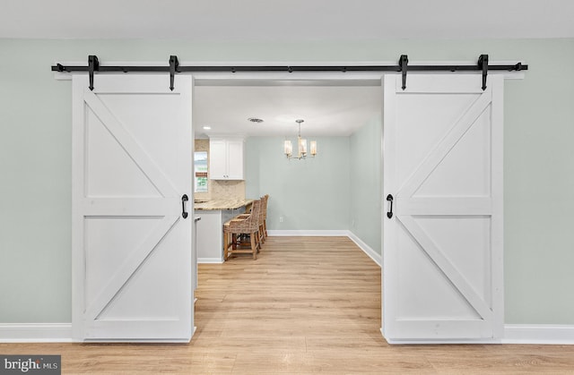 12542 Torquay Rd, Ocean City, MD 21842 - kitchen with a barn door, light wood finished floors, white cabinetry, baseboards, and decorative light fixtures