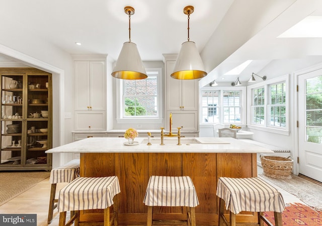 7006 Meadow Ln, Chevy Chase, MD 20815 - kitchen featuring light wood finished floors, white cabinetry, hanging light fixtures, an island with sink, and a kitchen bar