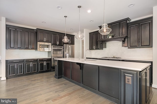 9073 Bear Branch Pl, Fairfax, VA 22031 - kitchen with appliances with stainless steel finishes, decorative backsplash, light wood-style floors, light countertops, and a large island with sink