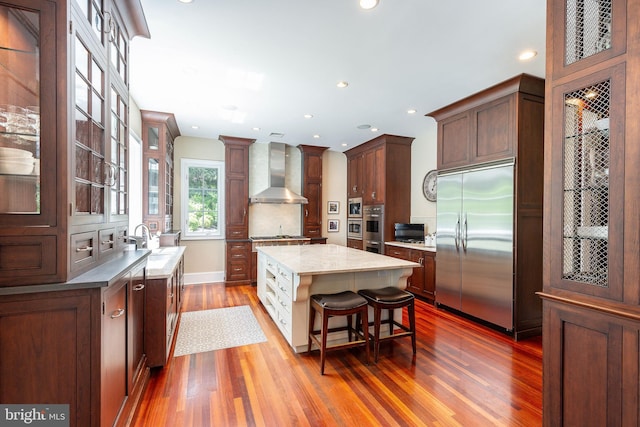 1412 Mount Pleasant Rd, Villanova, PA 19085 - kitchen featuring stainless steel appliances, wall chimney range hood, wood finished floors, glass insert cabinets, and a kitchen island