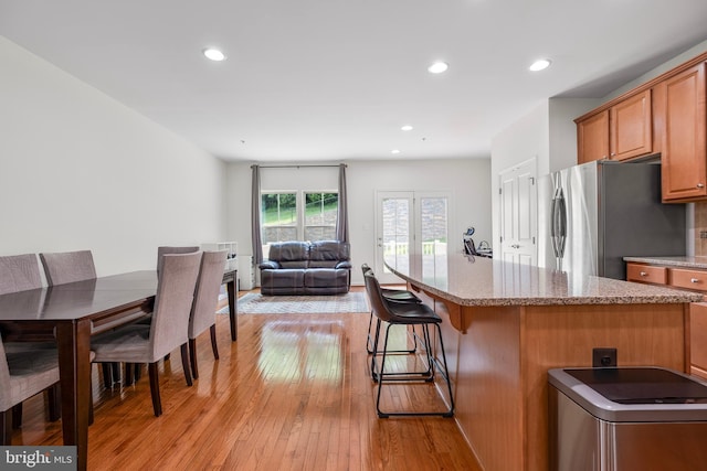 9161 Landon House Ln, Frederick, MD 21704 - kitchen with freestanding refrigerator, light wood-style flooring, a breakfast bar, light stone counters, and brown cabinets