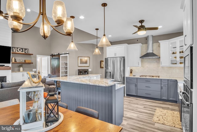 61 Bragg Dr, East Berlin, PA 17316 - kitchen with wall chimney exhaust hood, stainless steel appliances, a barn door, a ceiling fan, and light wood-style floors