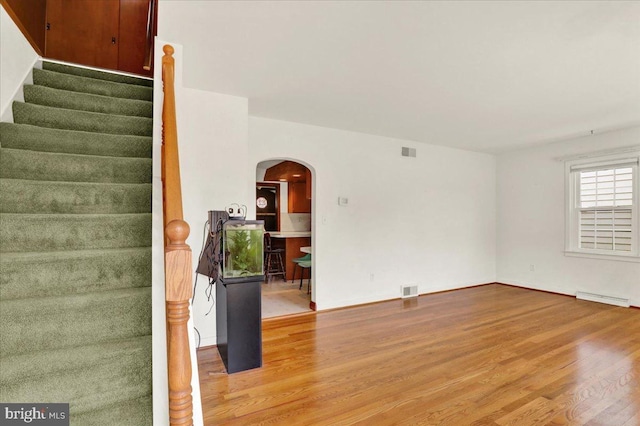 217 E Chestnut St, Cleona, PA 17042 - empty room featuring arched walkways, wood finished floors, stairs, and a baseboard heating unit