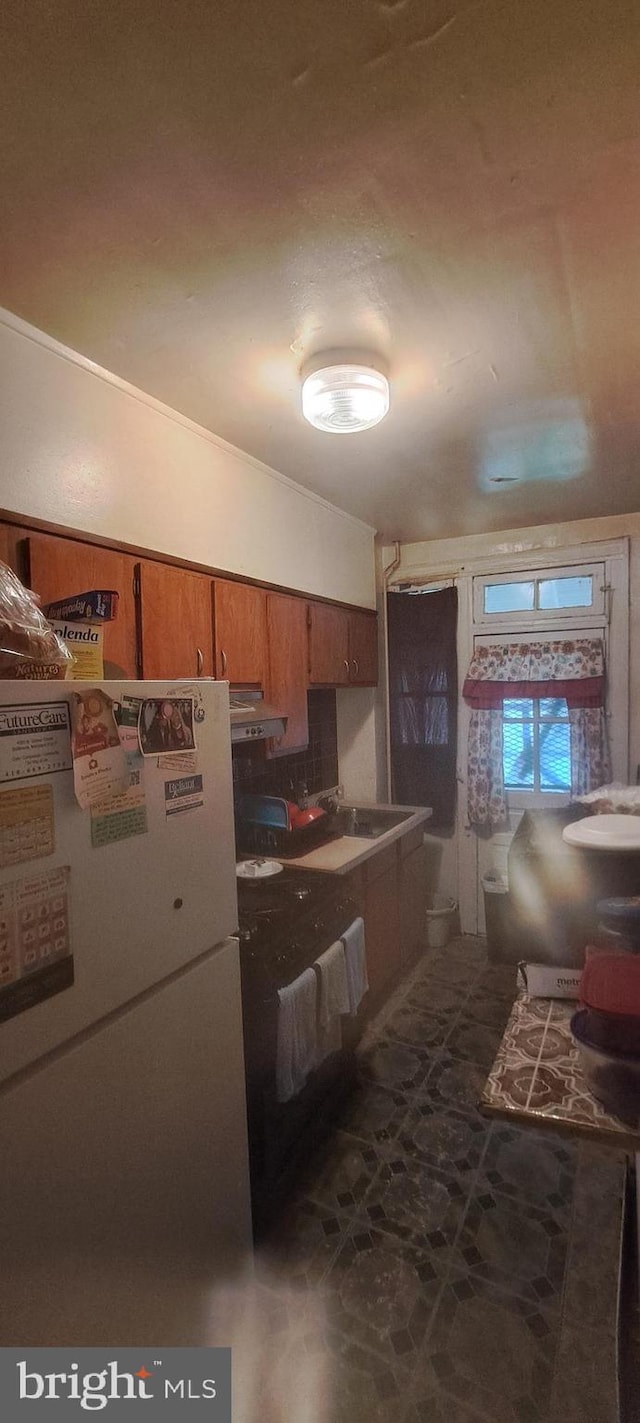 2207 W Lafayette Ave, Baltimore, MD 21216 - kitchen with freestanding refrigerator, brown cabinets, and under cabinet range hood
