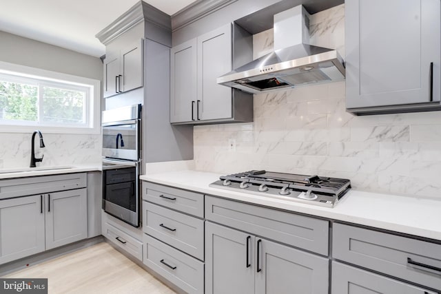 5002 Chalgrove Ave, Baltimore, MD 21215 - kitchen featuring wall chimney range hood, gray cabinets, a sink, appliances with stainless steel finishes, and tasteful backsplash