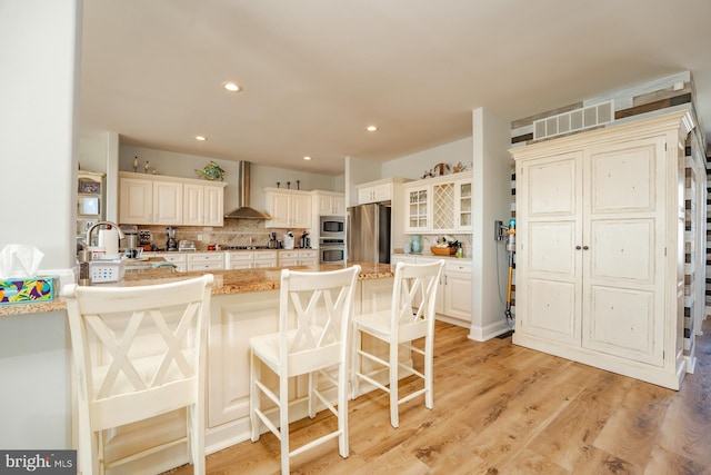 1107 Ocean Ave, Brigantine, NJ 08203 - kitchen featuring appliances with stainless steel finishes, wall chimney exhaust hood, a breakfast bar area, backsplash, and light stone counters