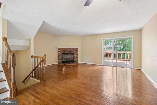 205 Quiet Ridge Ct, Pasadena, MD 21122 - unfurnished living room featuring wood finished floors, a textured ceiling, a ceiling fan, a brick fireplace, and baseboards