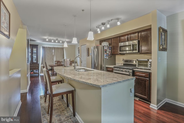 4613 Dillon St, Baltimore, MD 21224 - kitchen with appliances with stainless steel finishes, dark wood finished floors, dark brown cabinetry, a breakfast bar, and a kitchen island with sink