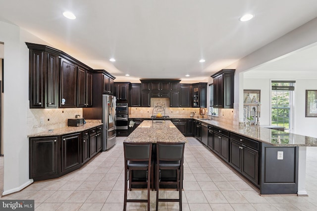 21550 Wild Timber Ct, Broadlands, VA 20148 - kitchen featuring a peninsula, backsplash, a center island, a sink, and light stone counters