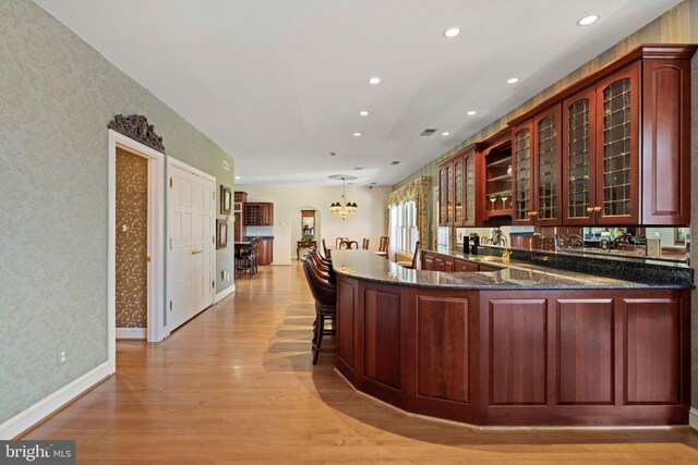 77 Lionheart Ter, Falling Waters, WV 25419 - kitchen featuring light wood-type flooring, wallpapered walls, glass insert cabinets, a chandelier, and dark stone countertops