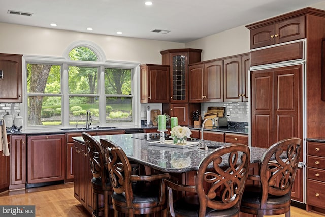 77 Lionheart Ter, Falling Waters, WV 25419 - kitchen featuring an island with sink, decorative backsplash, a breakfast bar area, dark stone counters, and glass insert cabinets