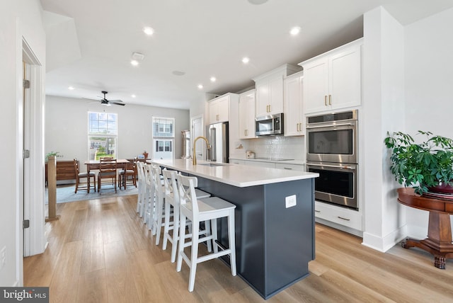 8790 Kensington Church St, Manassas, VA 20112 - kitchen with stainless steel appliances, a center island with sink, white cabinetry, light wood finished floors, and recessed lighting