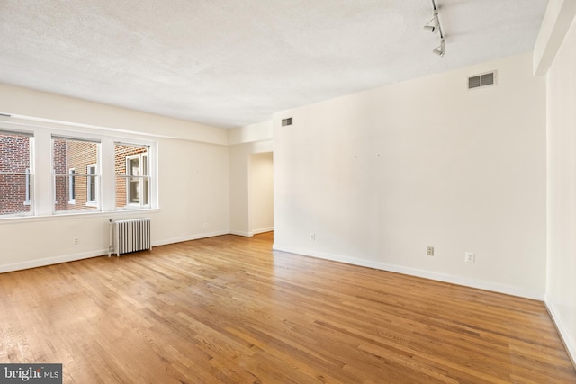 3901 Connecticut Ave NW Unit 406, Washington, DC 20008 - unfurnished room featuring radiator heating unit, light wood-style floors, rail lighting, baseboards, and a textured ceiling