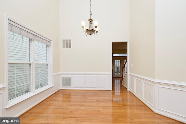 9573 5th Pl, Lorton, VA 22079 - unfurnished dining area featuring a chandelier, light wood-style floors, wainscoting, a towering ceiling, and a decorative wall