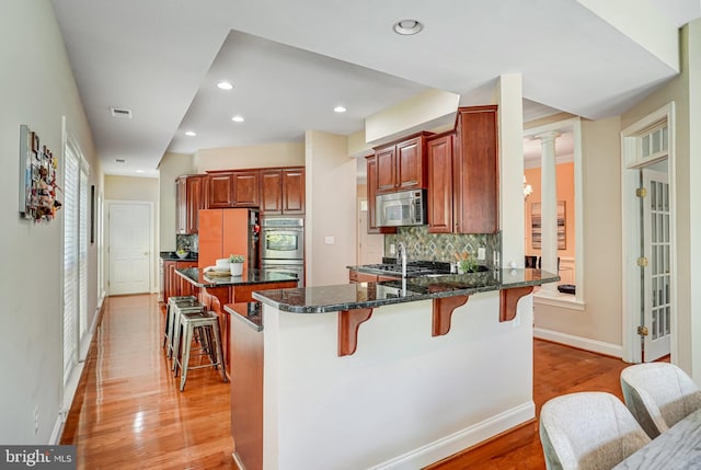 5968 Manorview Way, Alexandria, VA 22315 - kitchen featuring appliances with stainless steel finishes, a kitchen island, light wood-style floors, backsplash, and a breakfast bar