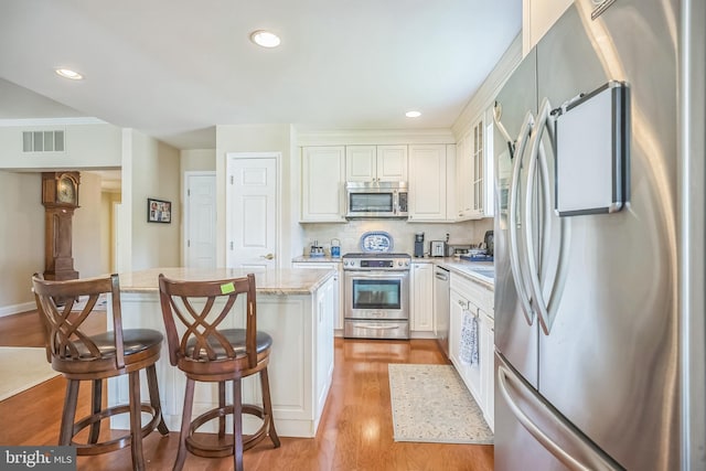1 Hedge Row Rd, Princeton, NJ 08540 - kitchen featuring appliances with stainless steel finishes, a center island, light wood-type flooring, white cabinets, and light stone counters