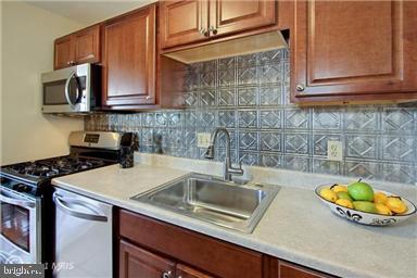 3515 Washington Blvd Unit 310, Arlington, VA 22201 - kitchen with appliances with stainless steel finishes, a sink, light countertops, backsplash, and brown cabinetry