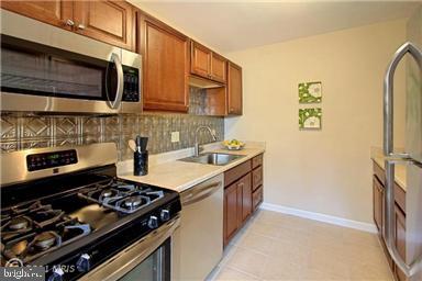 3515 Washington Blvd Unit 310, Arlington, VA 22201 - kitchen featuring appliances with stainless steel finishes, a sink, light countertops, tasteful backsplash, and brown cabinets