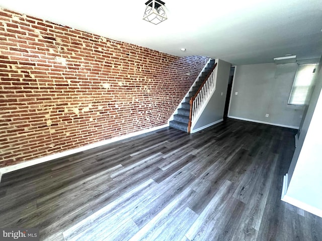 233 S Gilmor St, Baltimore, MD 21223 - unfurnished living room featuring baseboards, dark wood finished floors, stairs, and brick wall