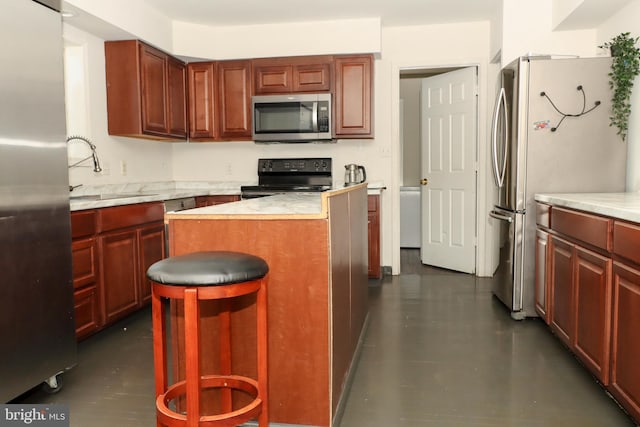 9216 Crandall Rd, Lanham, MD 20706 - kitchen featuring stainless steel appliances, light countertops, a kitchen island, a breakfast bar, and reddish brown cabinets