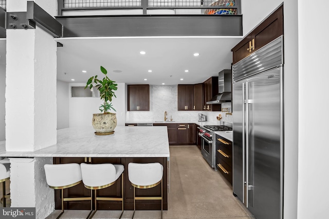 1220 Bank St Unit 304, Baltimore, MD 21202 - kitchen featuring premium appliances, wall chimney range hood, dark brown cabinetry, a peninsula, and a breakfast bar