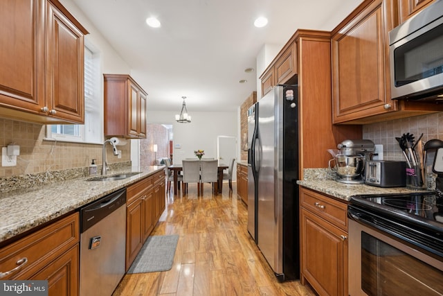 3032 Dillon St, Baltimore, MD 21224 - kitchen with stainless steel appliances, a sink, brown cabinets, light wood-style flooring, and decorative backsplash