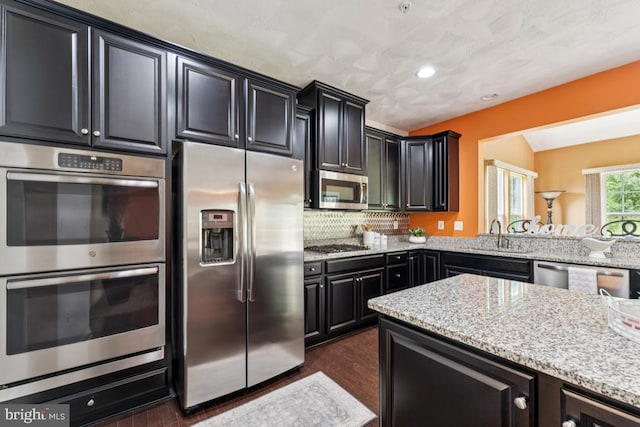 14302 Hidden Forest Dr, Accokeek, MD 20607 - kitchen featuring appliances with stainless steel finishes, a sink, dark cabinetry, light stone countertops, and dark wood-type flooring