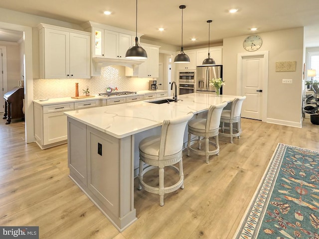 33016 Ethan Allen Dr, Rehoboth Beach, DE 19971 - kitchen featuring appliances with stainless steel finishes, a sink, white cabinetry, backsplash, and a large island with sink