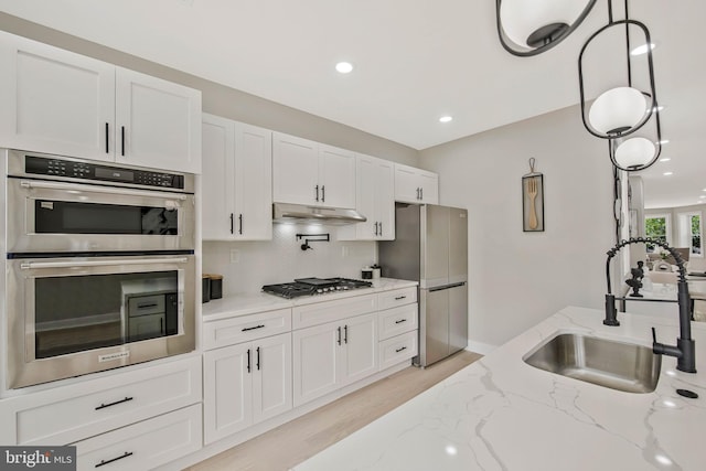 1713 4th St NW, Washington, DC 20001 - kitchen with appliances with stainless steel finishes, a sink, under cabinet range hood, white cabinetry, and light wood finished floors