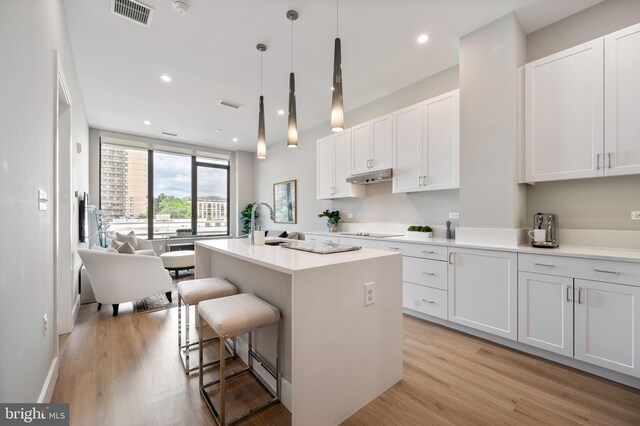 801 N Fairfax St Unit 314, Alexandria, VA 22314 - kitchen featuring black electric stovetop, white cabinets, light wood finished floors, a breakfast bar area, and an island with sink