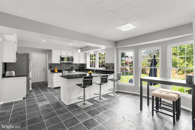 12407 Rousseau Ter, North Potomac, MD 20878 - kitchen featuring stainless steel microwave, white cabinetry, tasteful backsplash, dark countertops, and a breakfast bar
