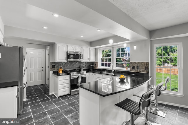 12407 Rousseau Ter, North Potomac, MD 20878 - kitchen featuring stainless steel appliances, a peninsula, dark countertops, white cabinets, and a breakfast bar