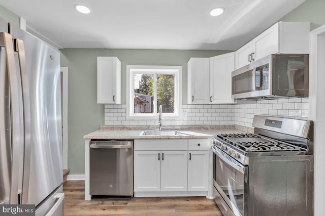 602 Market St, Gloucester City, NJ 08030 - kitchen featuring appliances with stainless steel finishes, a sink, white cabinetry, light wood-style flooring, and backsplash