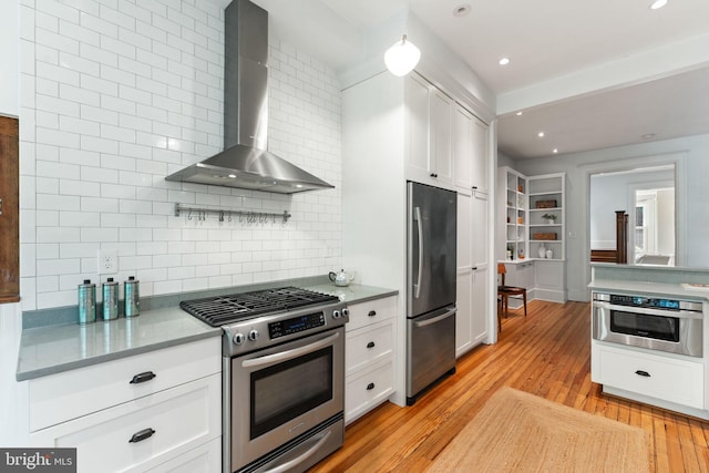 111 8th St SE, Washington, DC 20003 - kitchen featuring stainless steel appliances, wall chimney exhaust hood, backsplash, white cabinets, and light wood finished floors