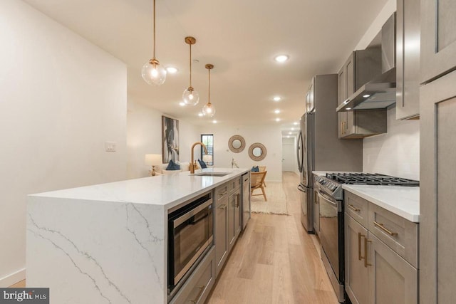 850 N 19th St Unit A, Philadelphia, PA 19130 - kitchen featuring appliances with stainless steel finishes, a sink, wall chimney range hood, light wood-style flooring, and a center island with sink
