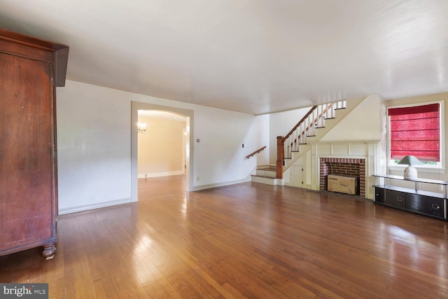 404 Clear Ridge Rd, Union Bridge, MD 21791 - unfurnished living room with wood-type flooring, arched walkways, stairs, a brick fireplace, and baseboards