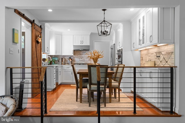 8017 Lake Pleasant Dr, Springfield, VA 22153 - kitchen with decorative backsplash, white cabinets, under cabinet range hood, light wood-type flooring, and a chandelier