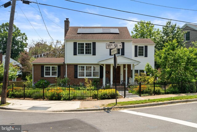 5600 11th St N, Arlington, VA 22205 - view of front facade with solar panels, a chimney, brick siding, a fenced front yard, and roof with shingles