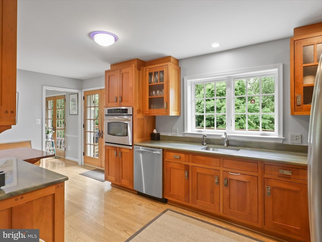 3725 N Delaware St, Arlington, VA 22207 - kitchen featuring appliances with stainless steel finishes, a sink, light wood-style floors, brown cabinetry, and glass insert cabinets