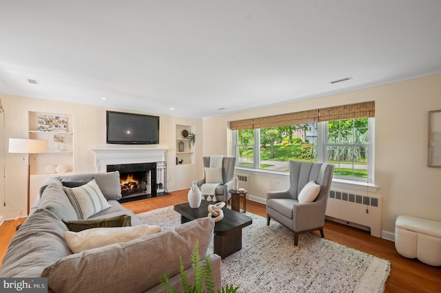 653 Broad Acres Rd, Penn Valley, PA 19072 - living area featuring radiator, a warm lit fireplace, wood finished floors, built in features, and baseboards