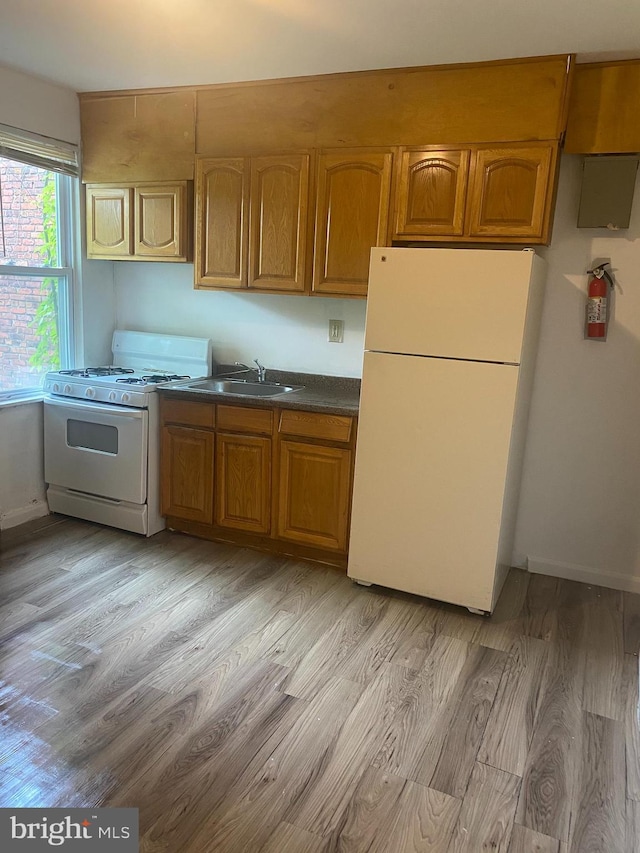 2919 Baker St, Baltimore, MD 21216 - kitchen featuring white appliances, a sink, light wood finished floors, brown cabinets, and dark countertops