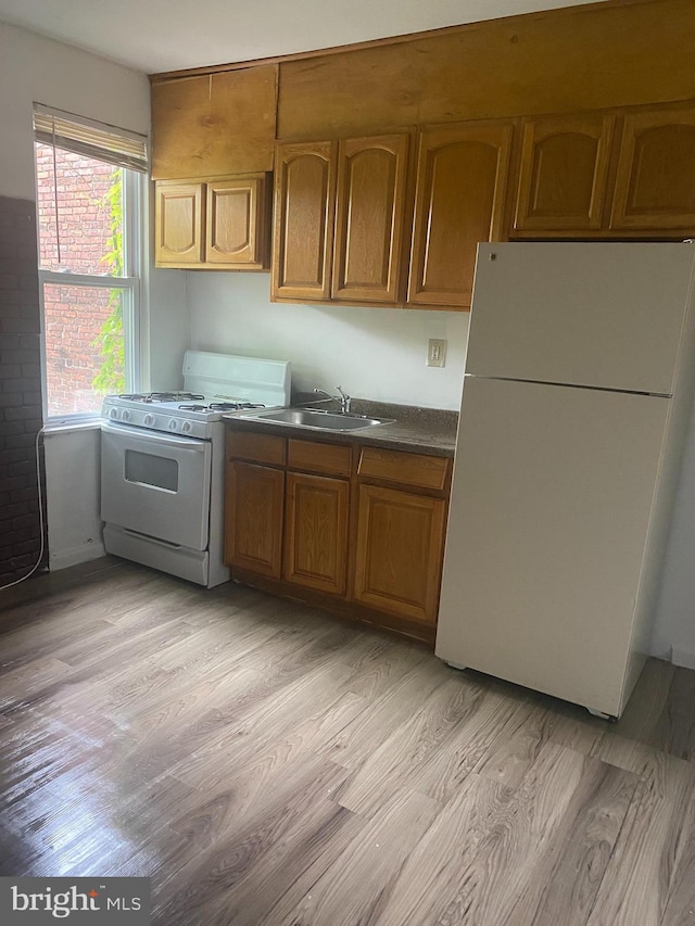 2919 Baker St, Baltimore, MD 21216 - kitchen with white appliances, light wood-style flooring, dark countertops, brown cabinets, and a sink