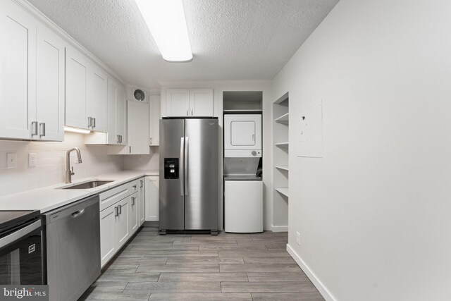 203 Yoakum Pkwy Unit 603, Alexandria, VA 22304 - kitchen featuring stainless steel appliances, a sink, stacked washer / dryer, white cabinets, and a textured ceiling